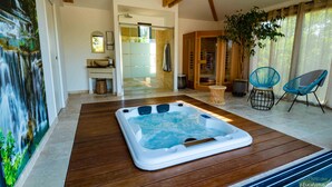 A spa area with a hot tub, wooden flooring, a large potted plant, and two blue chairs. - L'Oranger apartment, panoramic view of the village and hillsides (Le Plan-de-la-Tour)