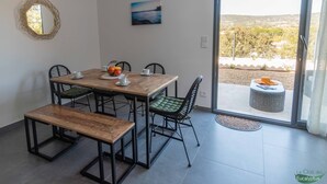 A dining area with a wooden table, four chairs, and a bench. There is a view of a landscape through a glass door. - L'Oranger apartment, panoramic view of the village and hillsides (Le Plan-de-la-Tour)