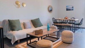 A modern living room with a sofa, coffee table, ottoman, and dining area with chairs and a table. - L'Oranger apartment, panoramic view of the village and hillsides (Le Plan-de-la-Tour)
