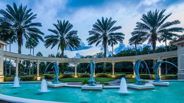 A fountain with dolphin sculptures in a landscaped area with palm trees and a sign reading "Emerald Island". - Extended Stay Retreat – Private Pool, Spa & Space for Everyone  (Kissimmee)