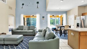 A spacious living area with a sofa set, ottoman, and a kitchen area with a refrigerator and counter. - Extended Stay Retreat – Private Pool, Spa & Space for Everyone  (Kissimmee)