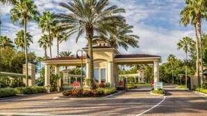 A covered entrance with palm trees, a gated driveway, and a clear sky. - Extended Stay Retreat – Private Pool, Spa & Space for Everyone  (Kissimmee)