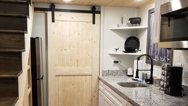 A kitchen with white cabinets, a granite countertop, a stainless steel microwave, and a wooden door.