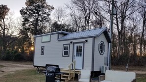A small, single-story mobile home with a front porch, a grill, and outdoor seating.