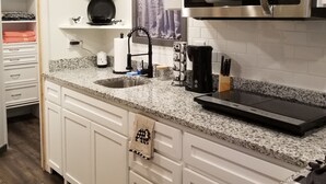 A modern kitchen with white cabinetry, a granite countertop, a stainless steel microwave, and a coffee maker.