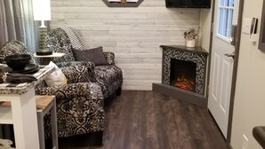 A cozy room with a wooden ceiling, a large window with a white bird, a fireplace, and a television mounted on the wall.