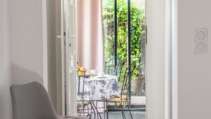 A hallway leading to a balcony with a table and chairs, a chair in the foreground, and a door with a phone on the wall. - L'Eucalyptus, mazet not overlooked, beautiful private outdoor space (Le Plan-de-la-Tour)