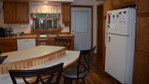 Una cocina con armarios de madera, un refrigerador blanco y una zona de comedor con mesa y sillas de madera.