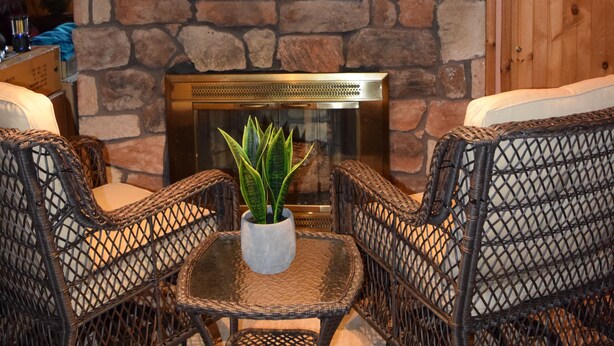 Una chimenea de piedra con un inserto eléctrico moderno, rodeada de sillones de mimbre y una pequeña mesa con una planta.