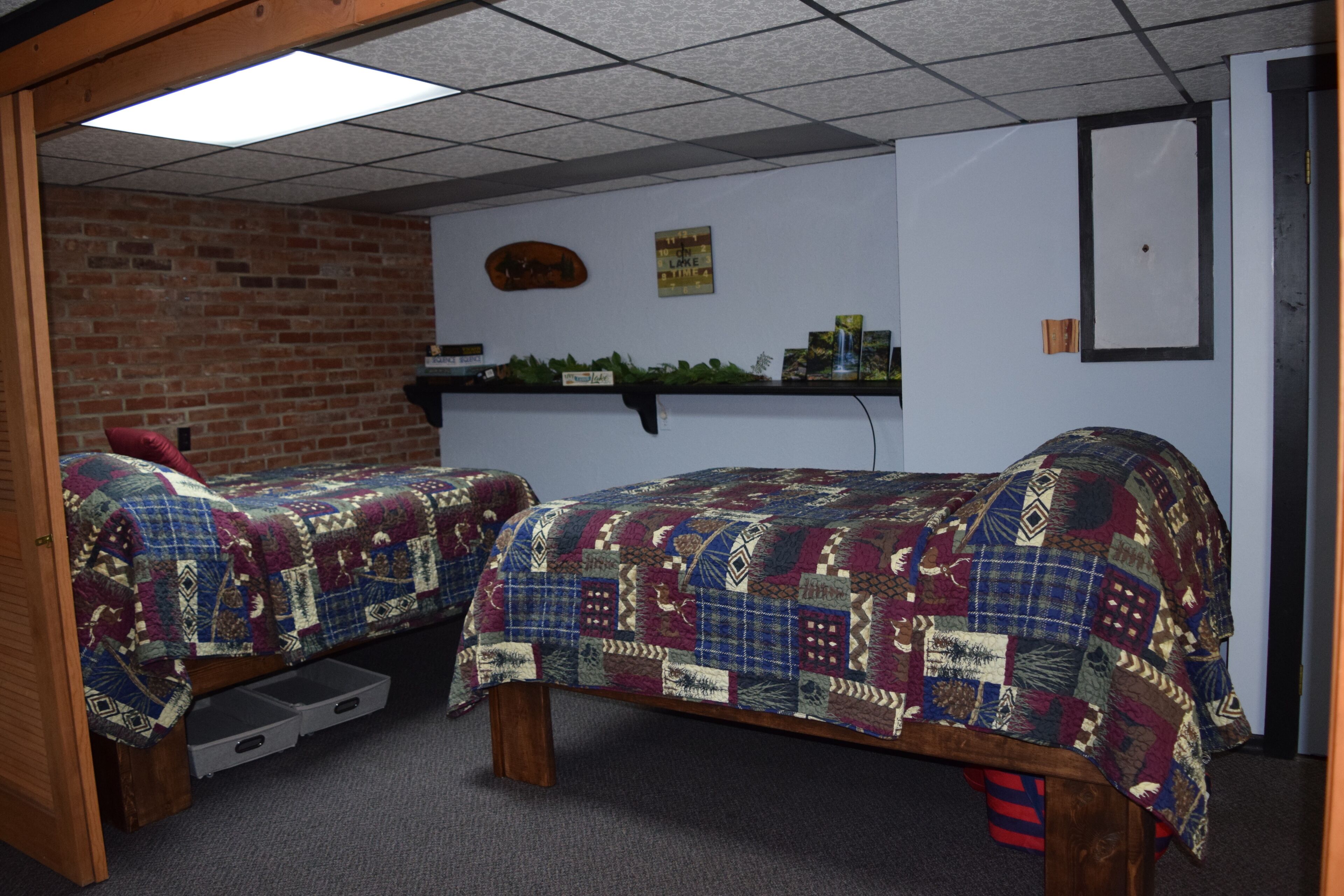A room with two beds, a brick wall, a shelf with items, and a door.