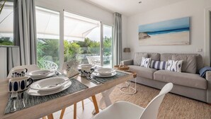 Un soggiorno moderno con zona pranzo, ampie finestre, un divano e un quadro raffigurante una spiaggia.