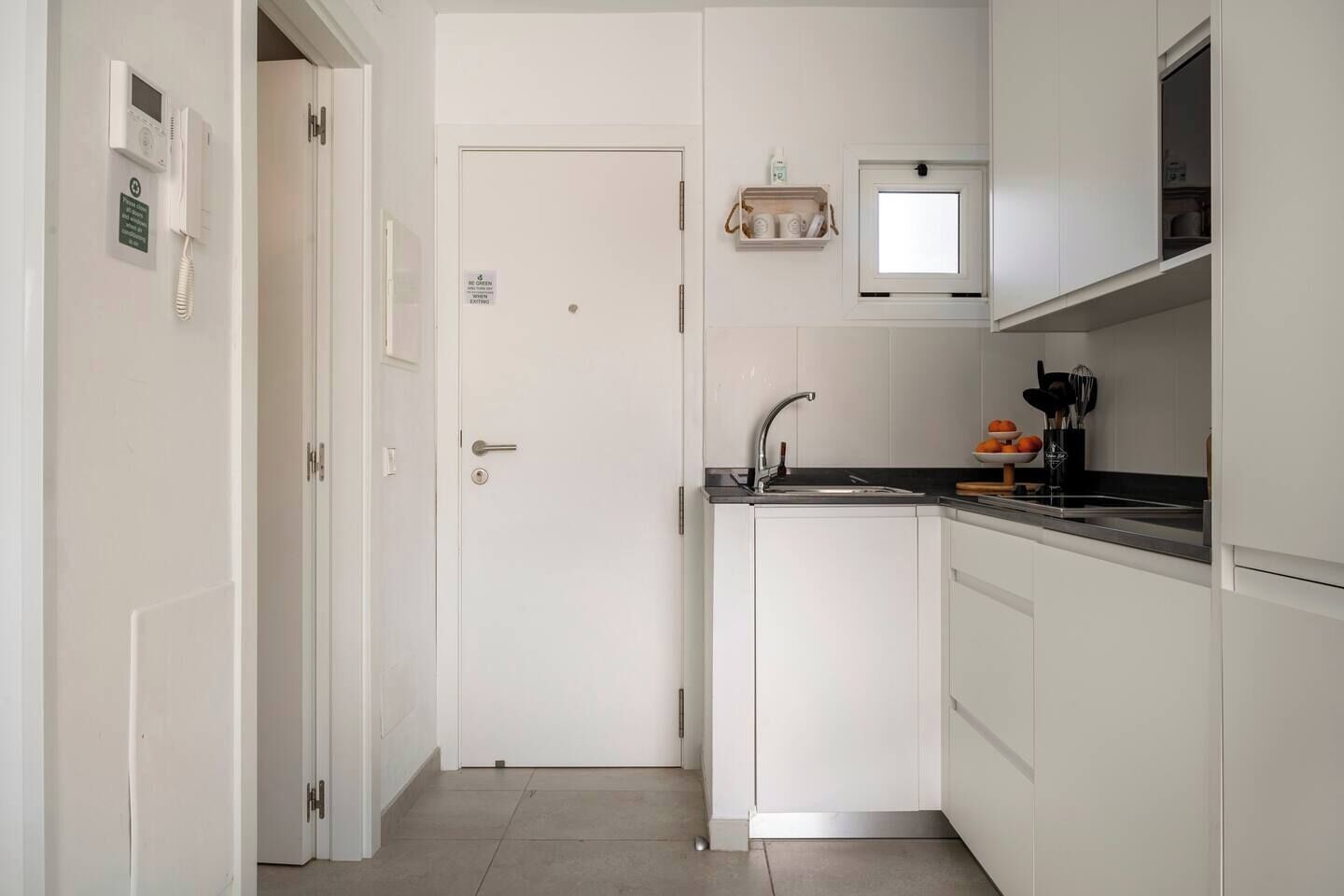 A compact kitchen with white cabinetry, a built-in sink, and a small window above the countertop.
