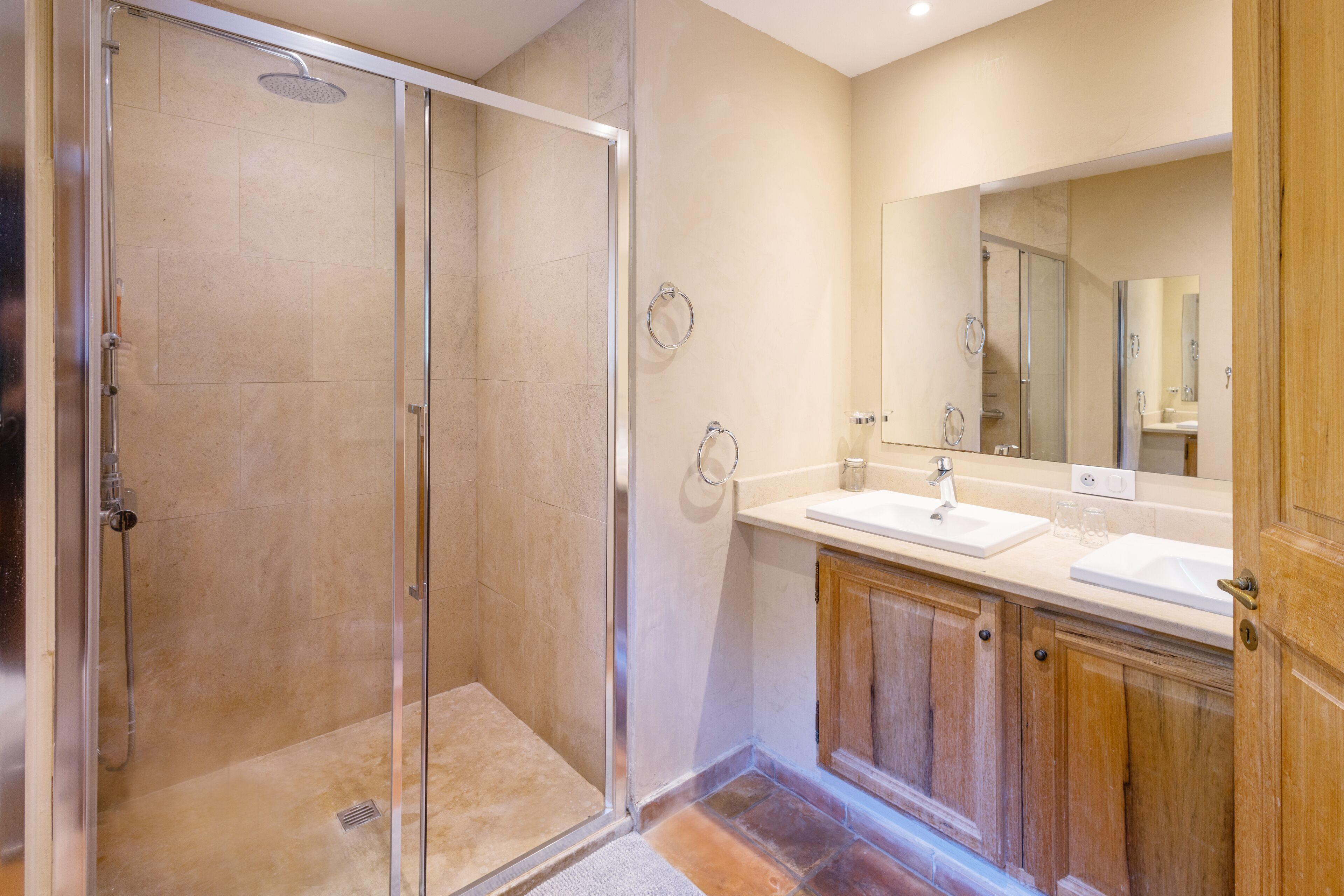 A modern bathroom with a glass-enclosed shower, a vanity with a mirror, and wooden cabinets.