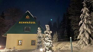 Un edificio cubierto de nieve con techo verde y paredes amarillas, con la leyenda "RENNHAUSL".