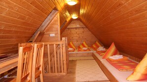Un interior de madera con techo inclinado, un banco de madera con almohadones y una silla de madera.