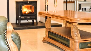 A wooden table with intricate carvings, a leather chair with metal studs, and a wood-burning stove in the background. - Glenshane Country House (Maghera)