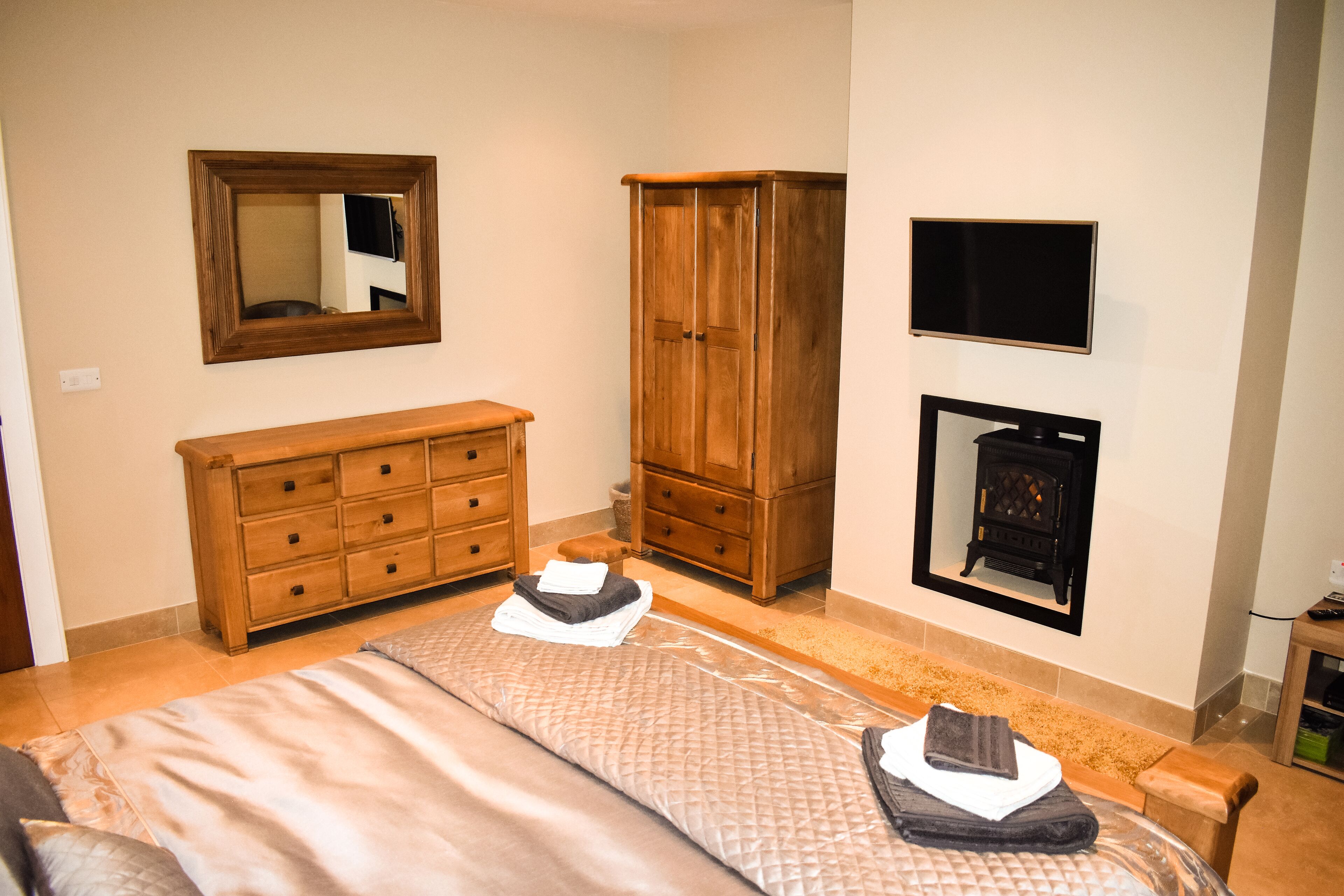 A bedroom with a bed, wooden dresser, wardrobe, and a fireplace.