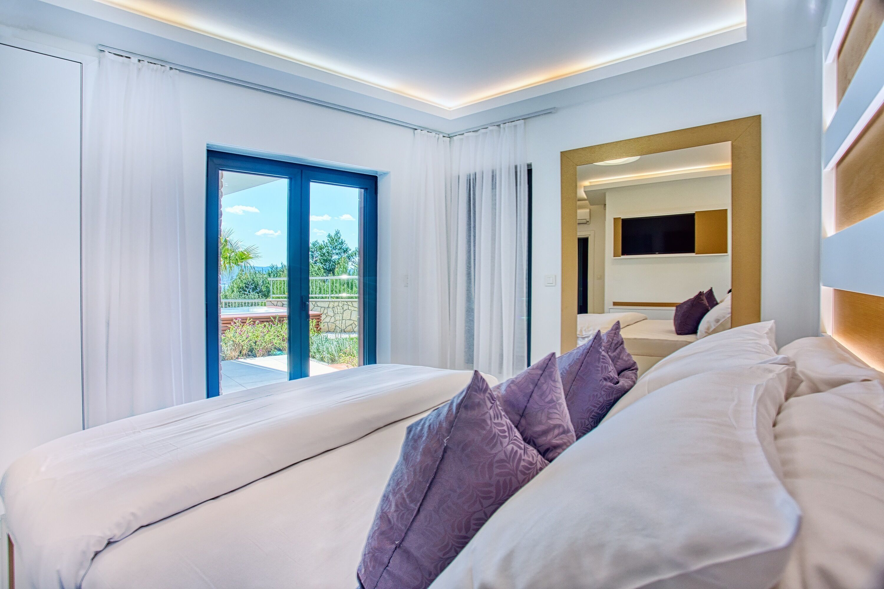 Una habitación de hotel moderna con una cama grande, un balcón con cortinas y un televisor.