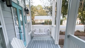 A covered porch with a table and chairs, a bench, and a view of the street and trees. - Family Beach Escape! Pool Access + Kayaks, Bikes & Paddleboard Included (Santa Rosa Beach)