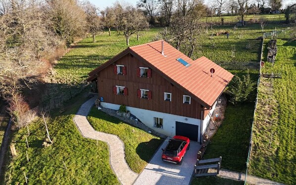 Een huis met twee verdiepingen, een rood dak, een garage en een rode auto die ervoor geparkeerd staat.