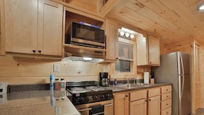 A compact kitchen with wooden cabinets, a stove, a microwave, and a refrigerator. - Martha Tiny Cabin at Lookout Close to Downtown (Chattanooga)