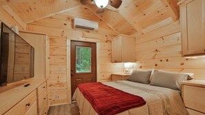 A wooden cabin bedroom with a bed, dresser, and a door leading outside. - Martha Tiny Cabin at Lookout Close to Downtown (Chattanooga)