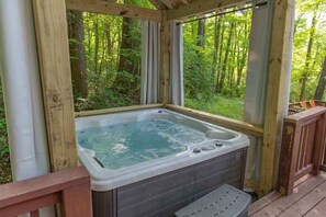 Un bain à remous installé sur une terrasse en bois, avec vue sur une forêt.