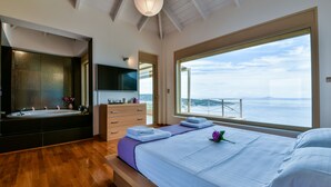 A modern bedroom with a large bed, a bathtub, and a view of the sea. - Infinite Blue Epidavros (Palaia Epidavros)