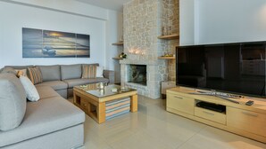 A modern living room with a stone fireplace, a large flat-screen TV, a sofa, and a coffee table. - Infinite Blue Epidavros (Palaia Epidavros)