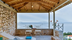 A covered outdoor seating area with stone walls, a view of the sea, and a wooden ceiling. - Infinite Blue Epidavros (Palaia Epidavros)
