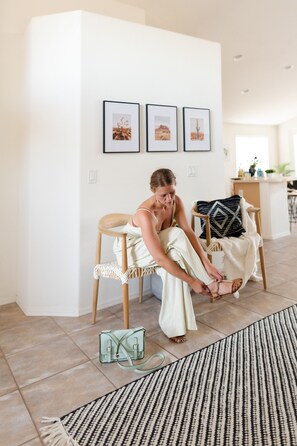 A woman sitting on a chair in a room with a tiled floor, a patterned rug, and framed pictures on the wall. - Sunny Desert Escape with Heated POOL! Near Spring Training, Stadium & Westgate (El Mirage)