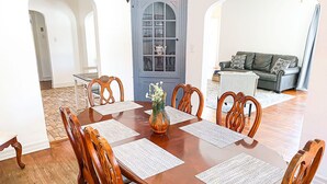 A dining area with a wooden table and chairs, a blue door with a window, and a living room in the background. - Cardinal House: Foseball, Sunroom, 6ft Fence, King Bed, Near Hospital & BassPro (Springfield)