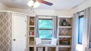 A bedroom with a built-in bookshelf, a ceiling fan, a window with curtains, and a bedside table with a lamp. - Cardinal House: Foseball, Sunroom, 6ft Fence, King Bed, Near Hospital & BassPro (Springfield)