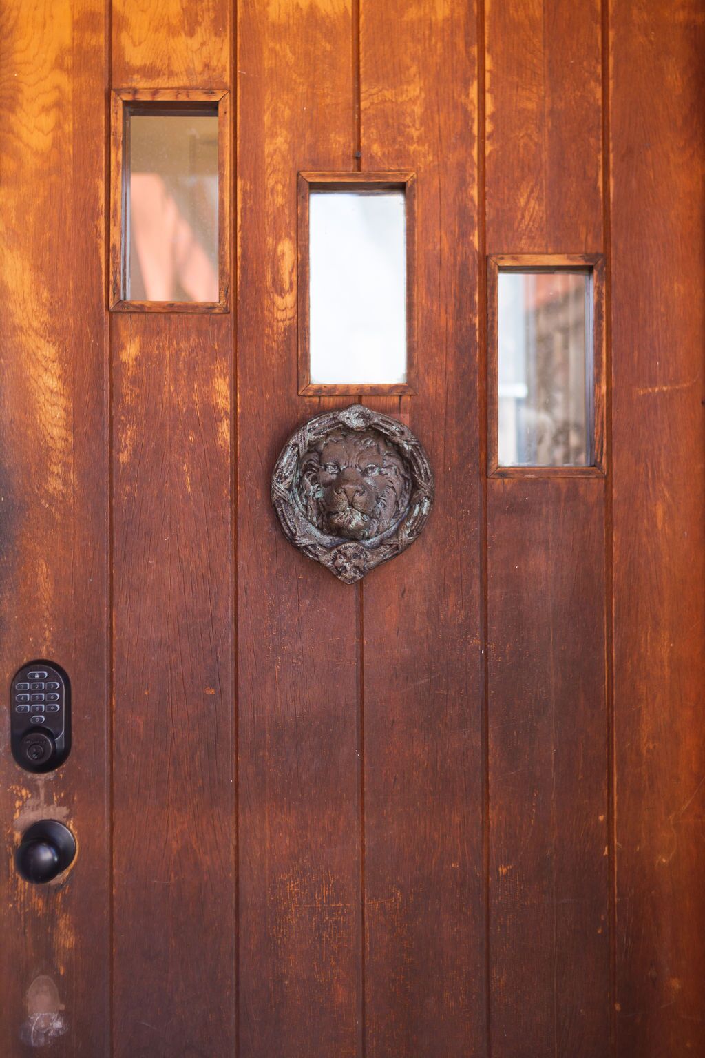 A wooden door with a lion head knocker, two small windows, and a keypad lock.