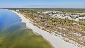 Oversigtsbillede af et kystnært boligområde med ejendomme direkte til stranden, en sandstrand og krystalklart hav.