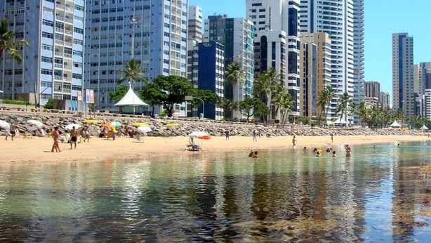 A beach with people, a sandy shore, and tall buildings in the background. - Furnished apartment on Avenida Boa Viagem, beachfront condominium. (Recife)