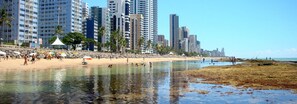 Uma praia com pessoas, areia e edifícios altos ao fundo.