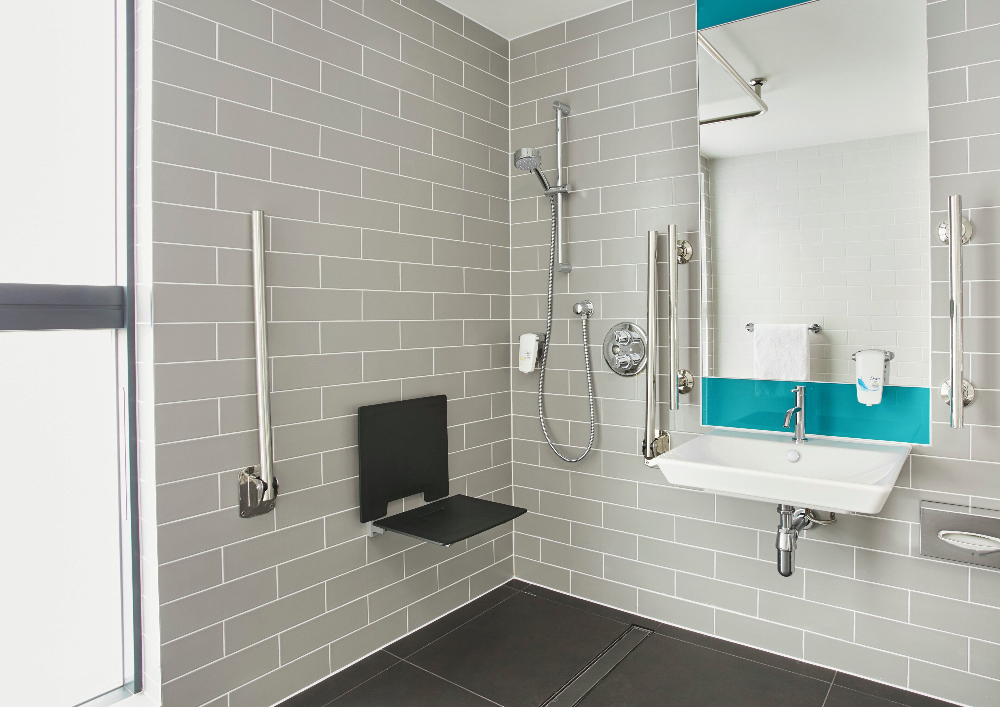 Ein modernes Badezimmer mit grauen Fliesenwänden, einem schwarzen Regal, einem weißen Waschbecken mit blauer Akzentfarbe und einer Handbrause.