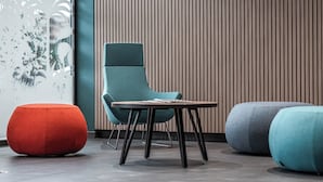 A modern interior with a teal chair, a wooden table, and two ottomans in red and blue. - Holiday Inn Express Ajaccio by IHG (Ajaccio)