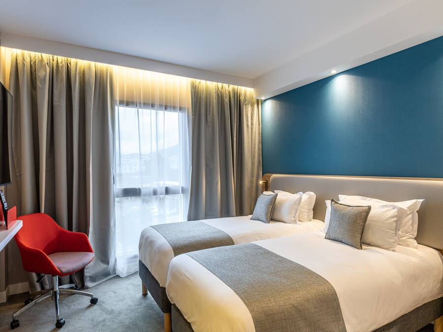 A hotel room with a bed, a desk with a chair, and a TV.