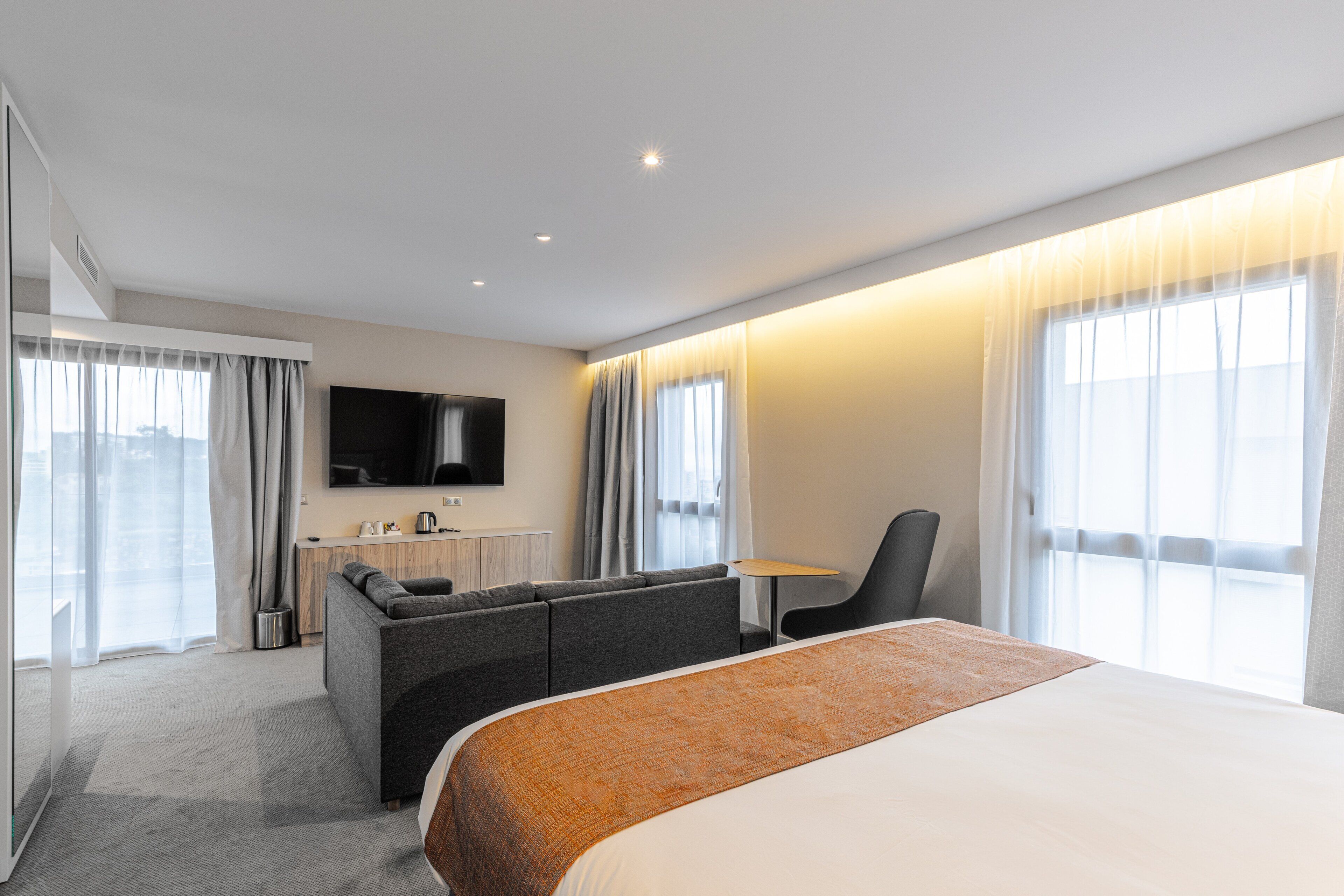 Une chambre d’hôtel avec un lit, un canapé, une télévision, un bureau et une fenêtre avec des rideaux.