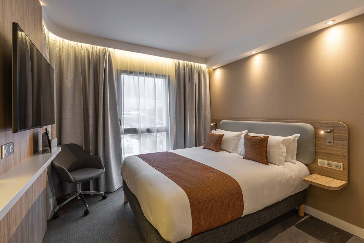 A modern hotel room with a large bed, a desk, and a TV.