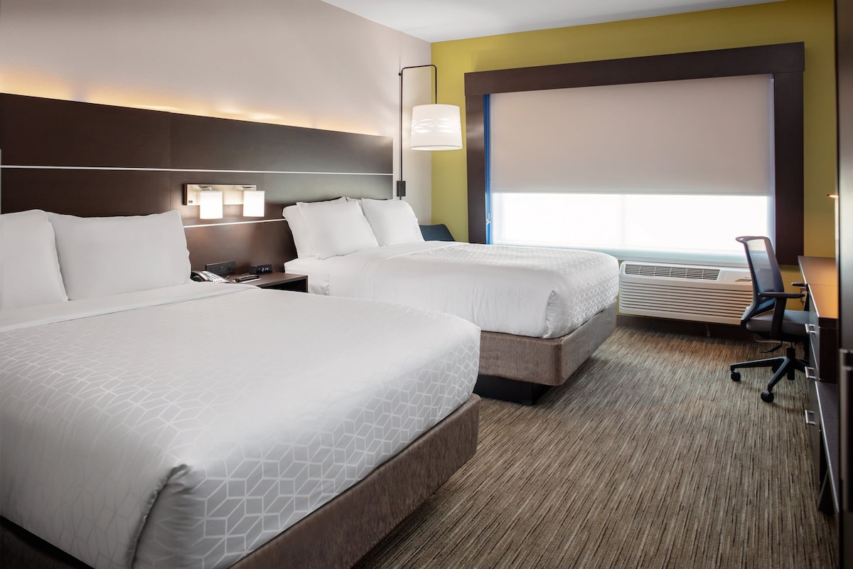 Een hotelkamer met twee bedden, een bureau, een stoel, een lamp en een groot raam met uitzicht.