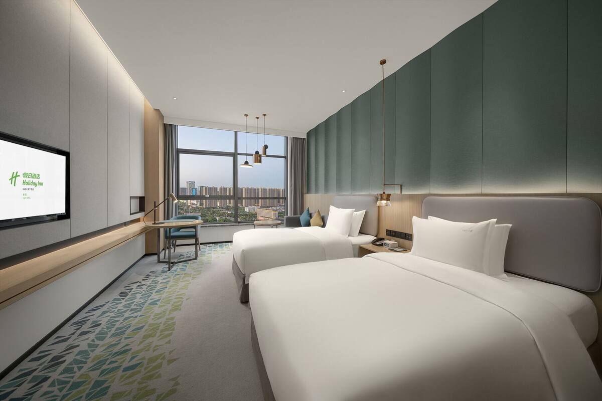 Une chambre d’hôtel moderne avec deux lits, un bureau et une grande fenêtre donnant sur la ville.