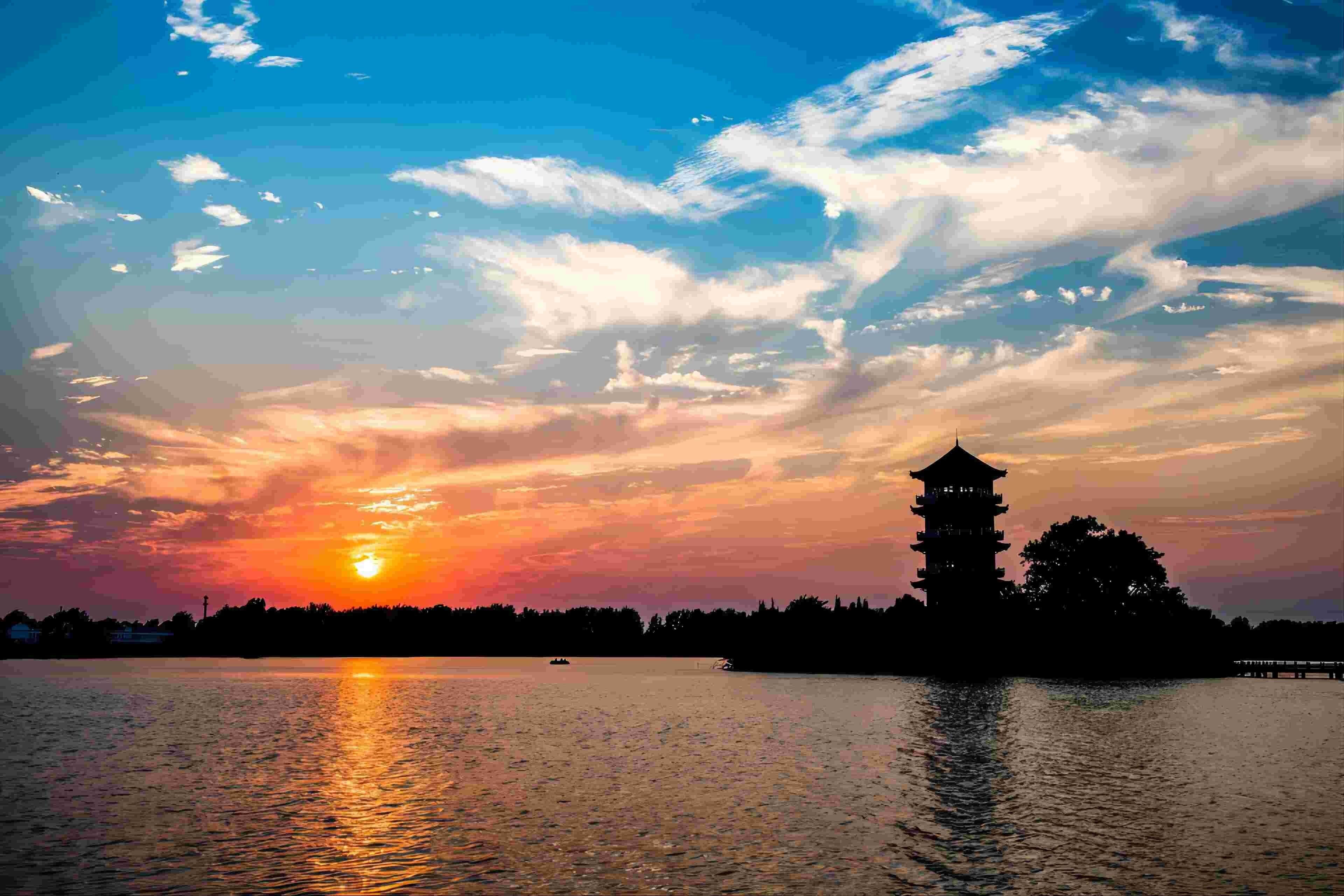 Un coucher de soleil paisible sur un lac calme, avec une tour de style pagode se détachant sur le ciel.