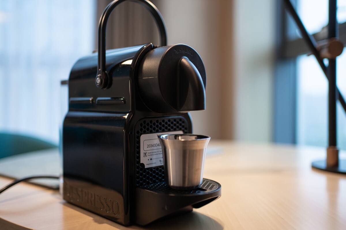 Une machine à café Nespresso avec un porte-tasse, posée sur une surface en bois.