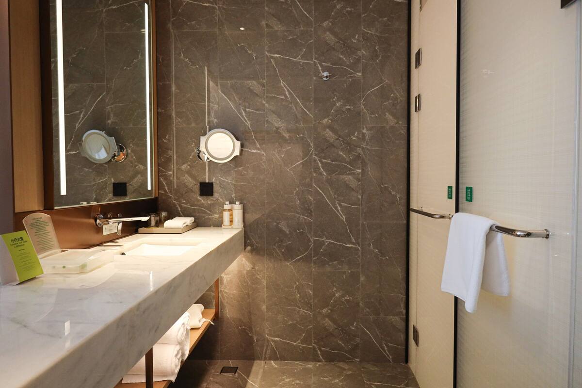 Une salle de bain avec un plan de toilette en marbre, un lavabo, un miroir, un porte-serviettes et un espace douche.