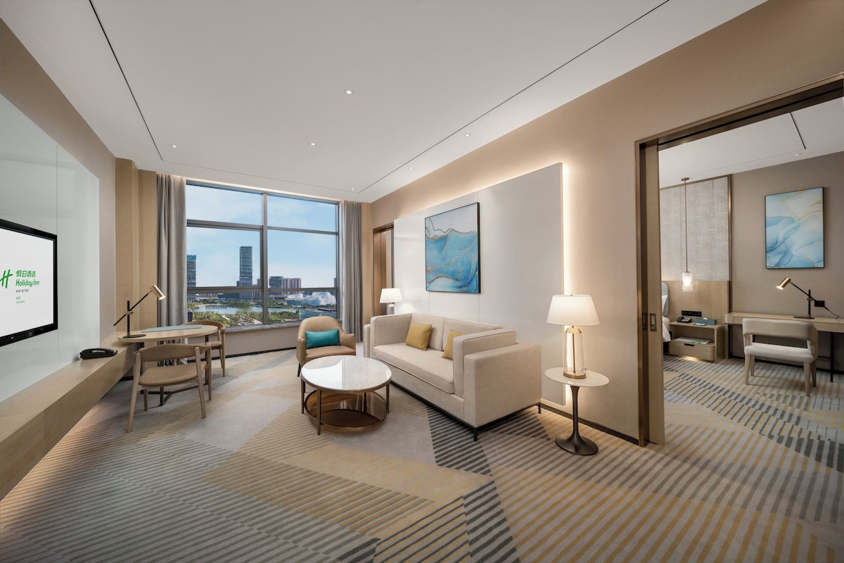 Et moderne hotelværelse med et stort vindue, en sofa, et sofabord, et skrivebord og et spejl.