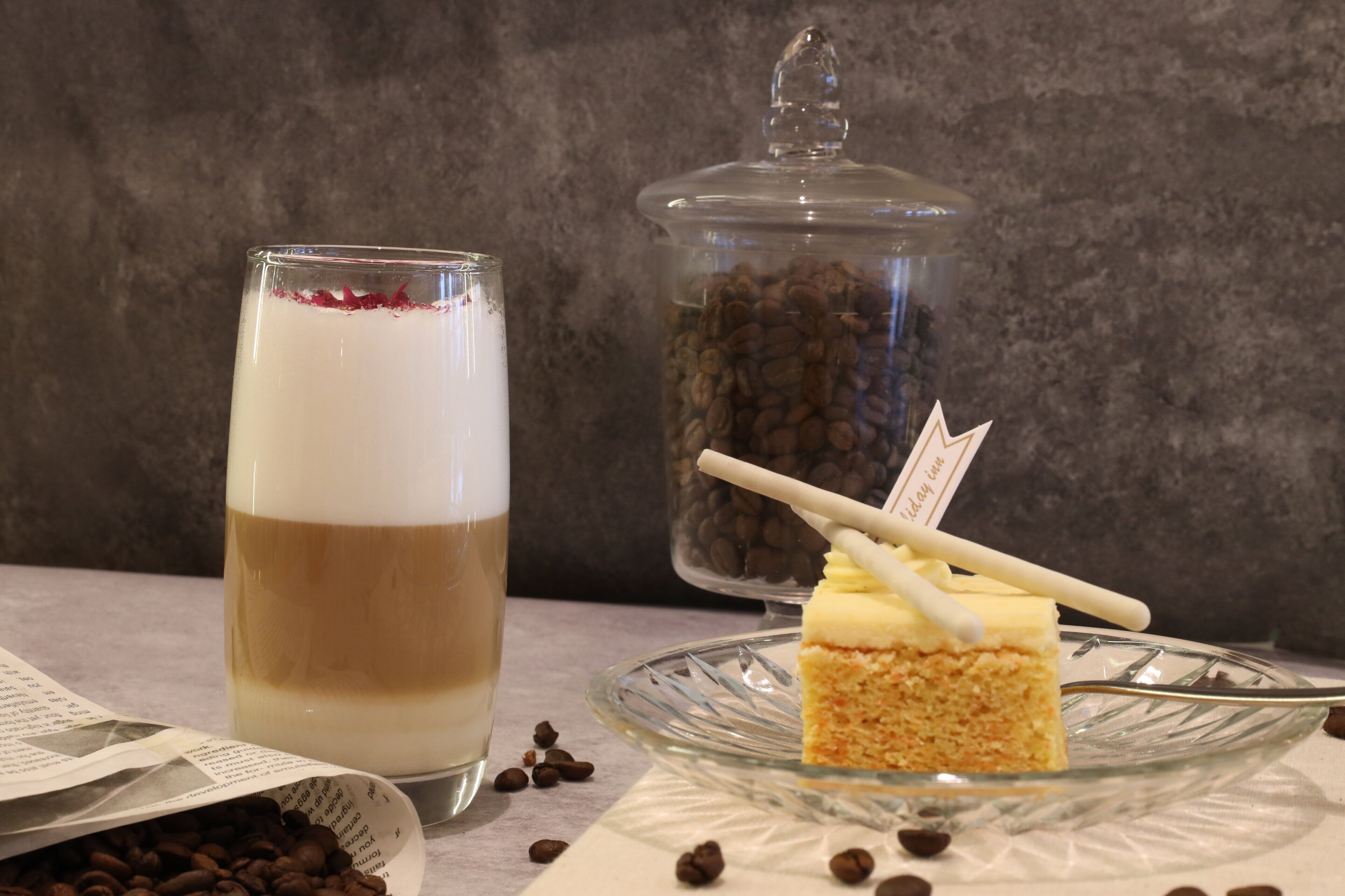 Un vaso con una bebida en capas, un tarro de granos de café y una porción de pastel sobre un plato de vidrio.