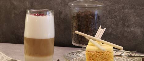 Un vaso con una bebida en capas, un tarro de granos de café y una porción de pastel sobre un plato de vidrio.